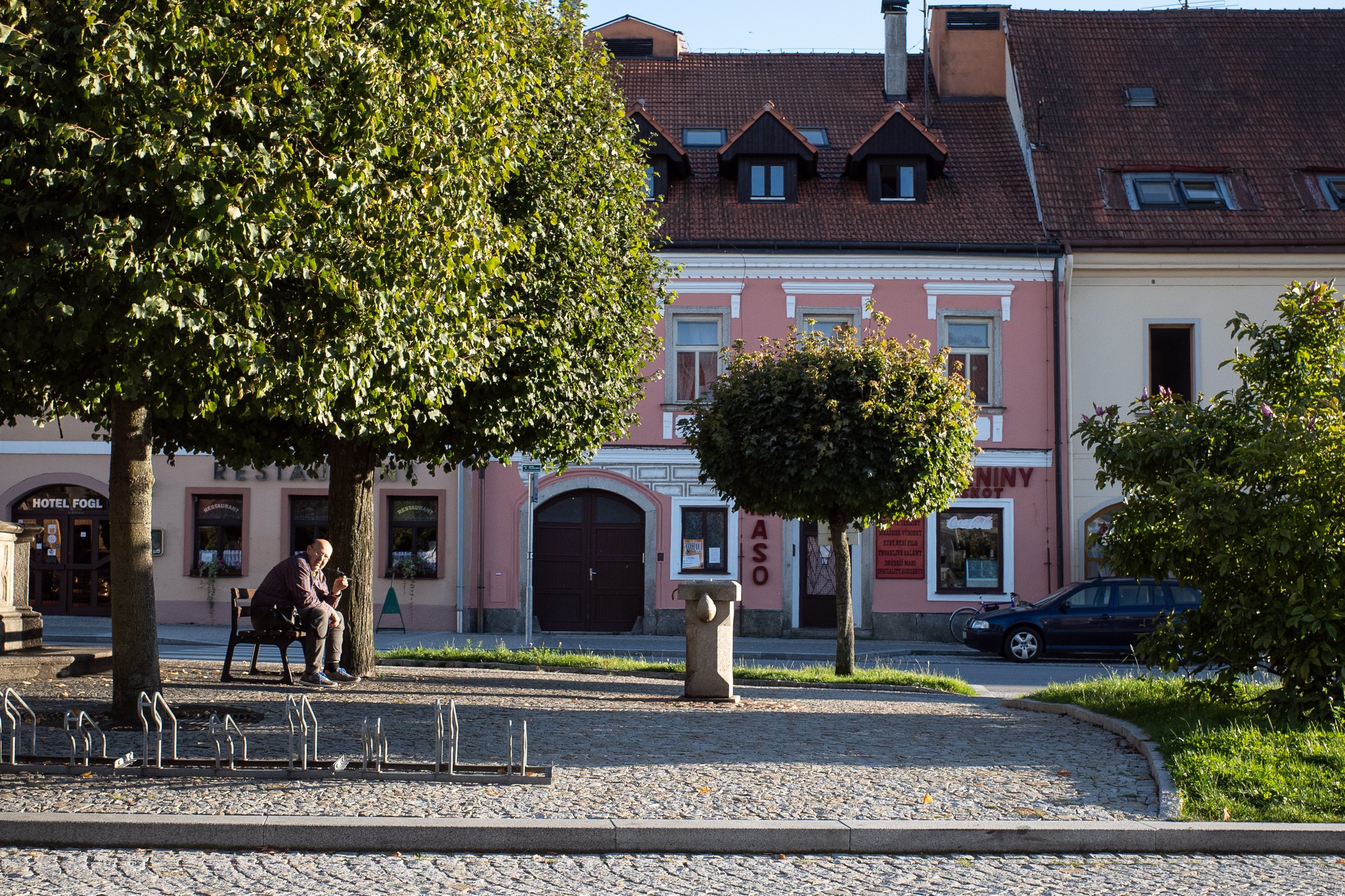 Nachmittag am Hauptplatz: Hotel Fogl, rosa Fassaden, ein Mann auf der Bank